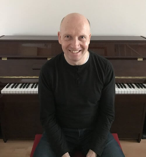 Paul Barnes, professional piano tuner, sitting in front of an upright piano